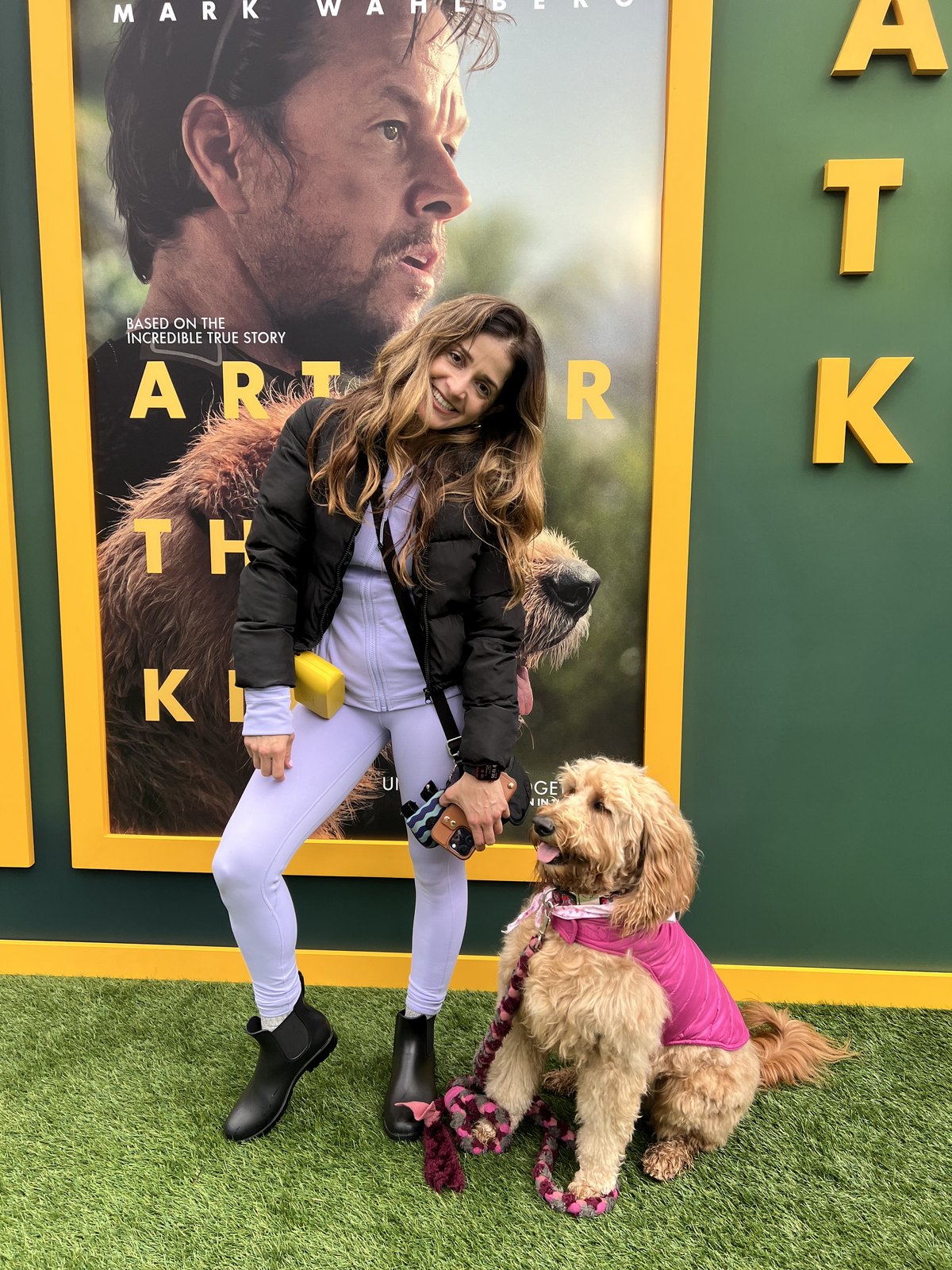 Lauren Pena hugging Peach the Goldendoodle in front of the Arthur the King poster
