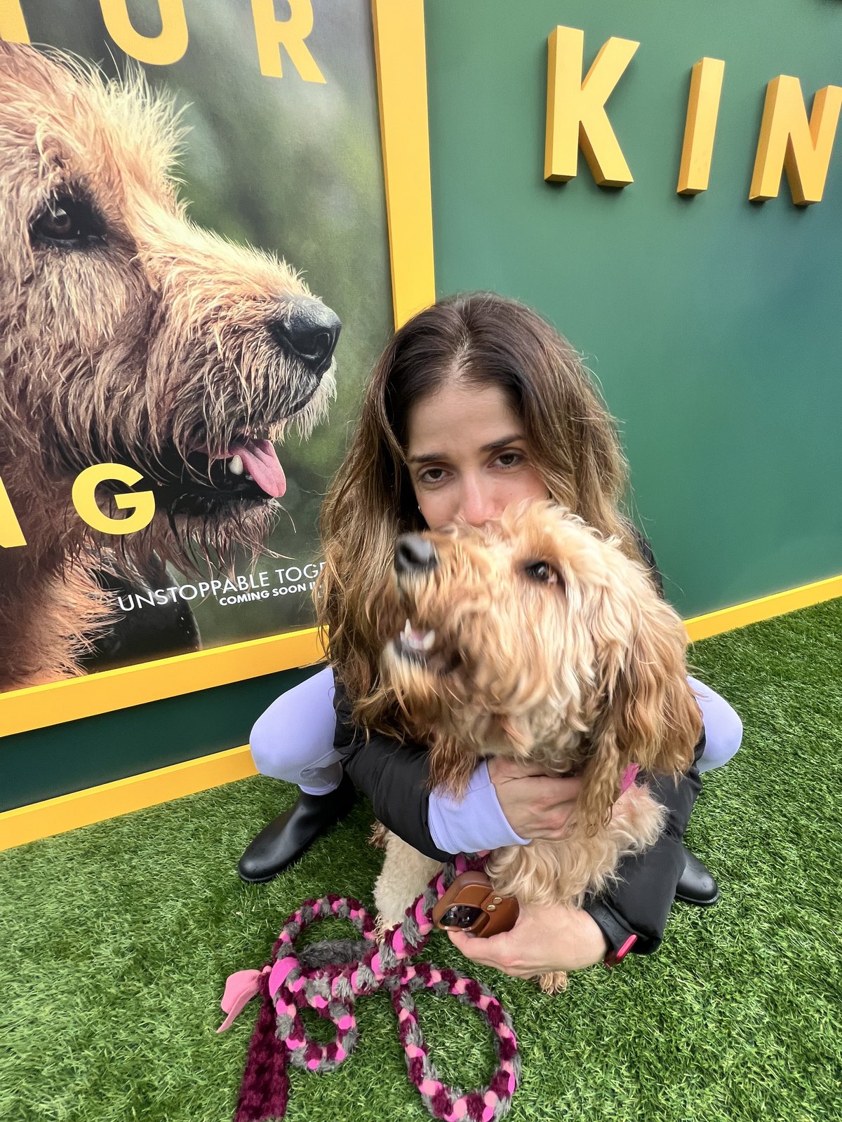 Peach the Goldendoodle with Lauren Pena in front of the Arthur the King film poster