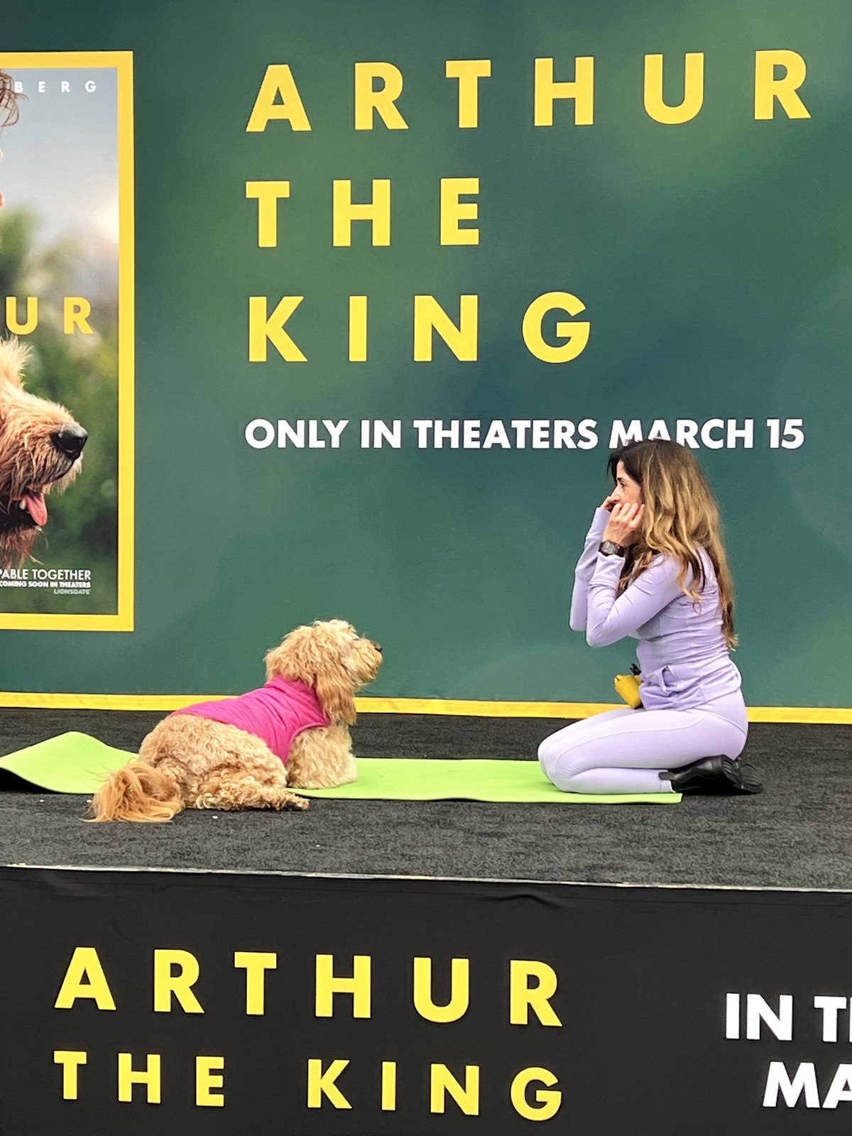 Lauren Pena kneeling in prayer hands facing Peach the Goldendoodle on a yoga mat on the Arthur the King event stage
